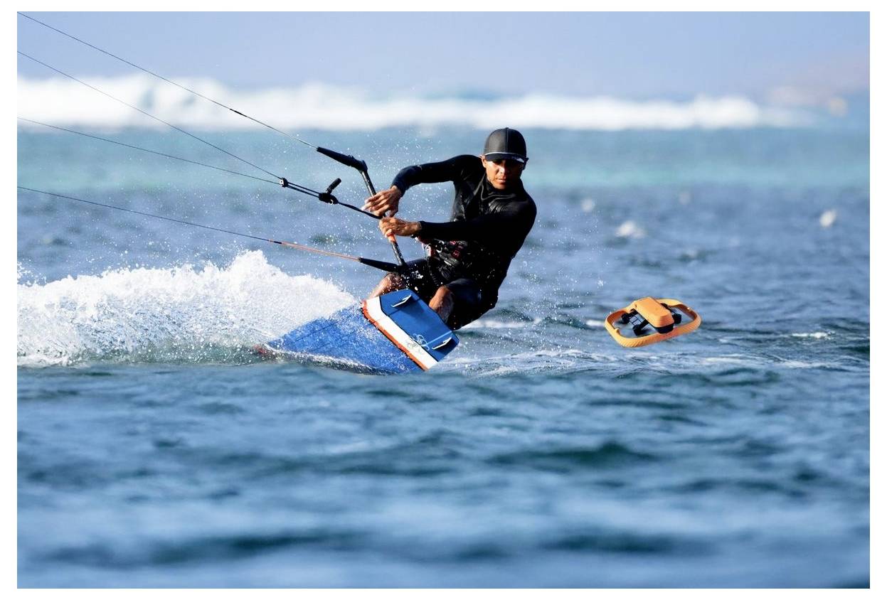 Un kitesurfeur en combinaison de plongée et casque ride à travers des eaux océaniques agitées, se penchant fortement tandis que la planche rase la surface.