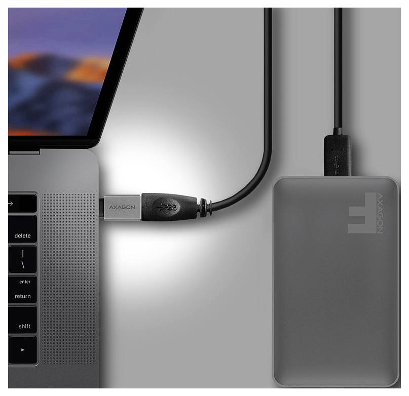 Ordinateur portable connecté par câble à un disque dur externe AXAGON gris ou un concentrateur situé à côté de lui sur un bureau.