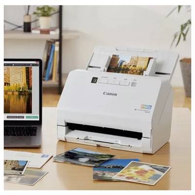 Imprimante photo Canon imprimant des images depuis un ordinateur portable, avec plusieurs photos imprimées dispersées sur un bureau.
