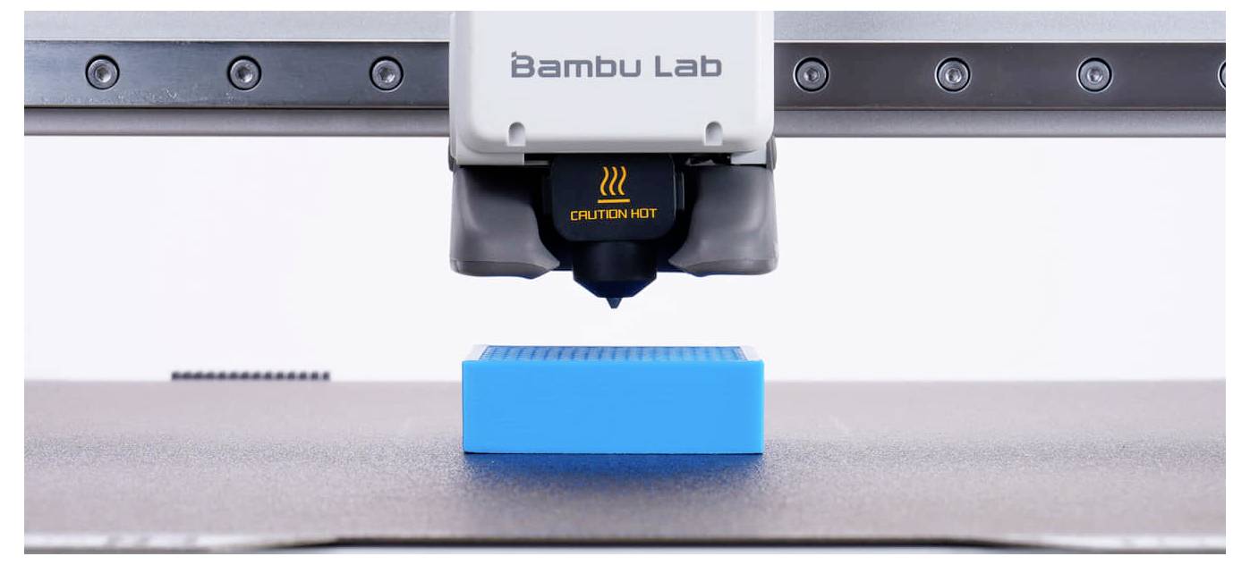Buse d'imprimante 3D Bambu Lab imprimant un bloc rectangulaire bleu sur le plateau de construction.