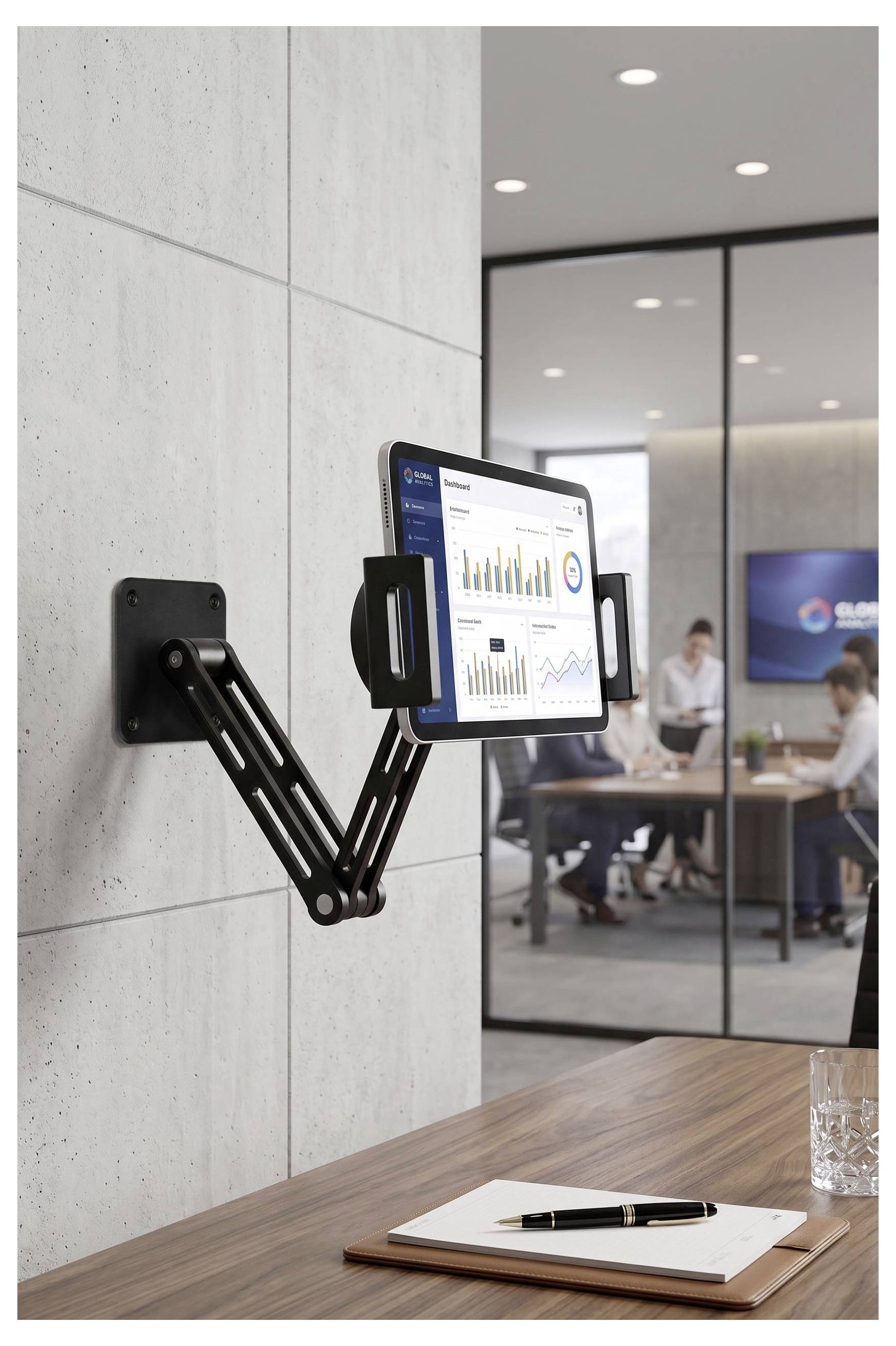 Bras de moniteur ajustable monté au mur tenant un écran avec des graphiques dans une salle de réunion de bureau moderne, au-dessus d'un bureau avec un bloc-notes et un stylo.