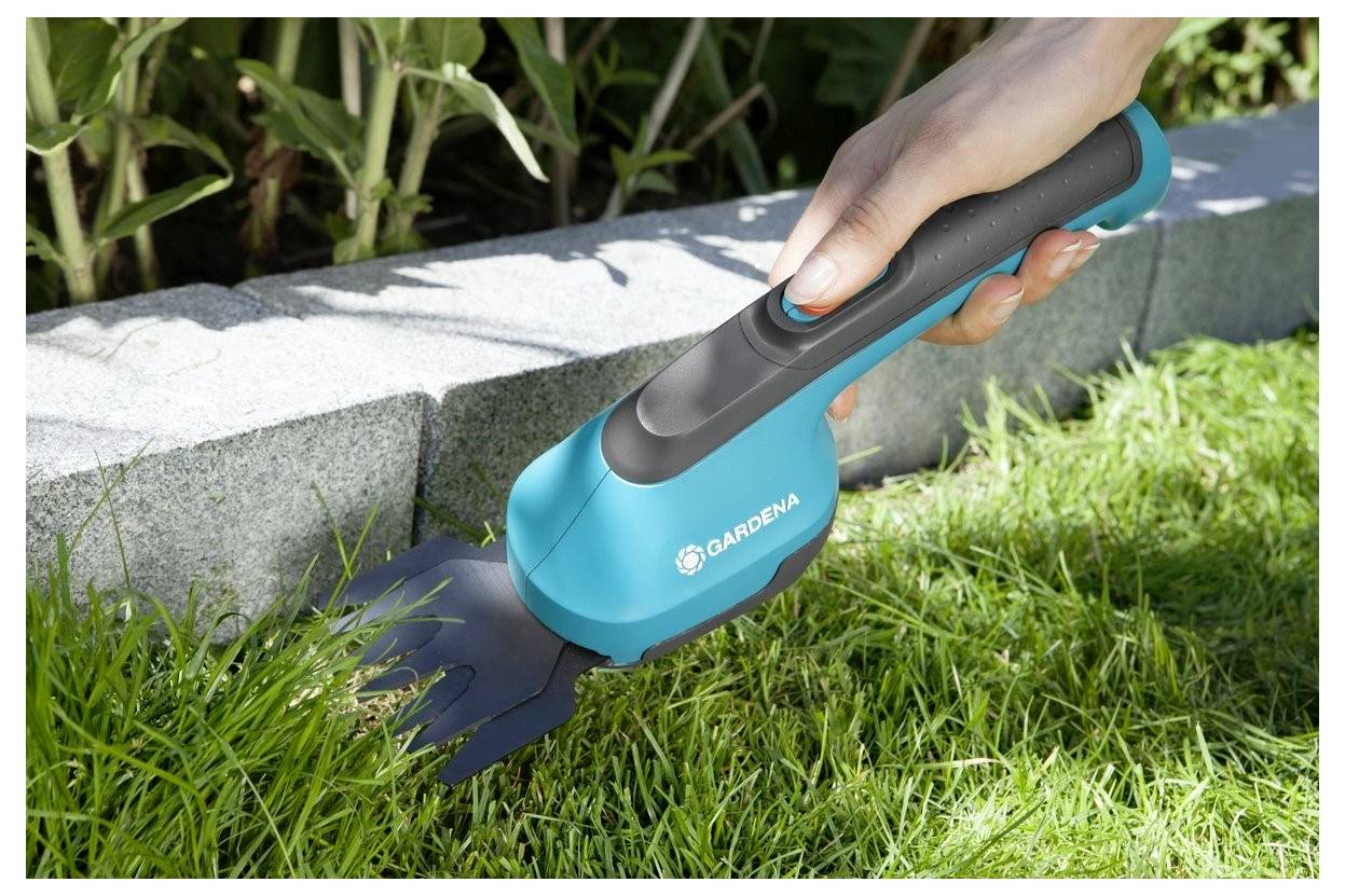 Une femme agenouillée sur l'herbe utilise un petit taille-bordure électrique bleu pour tailler la pelouse le long d'un parterre de fleurs.