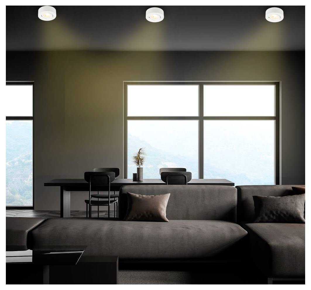 Salon moderne avec un canapé sectionnel foncé face à une table à manger et de grandes fenêtres avec une lumière extérieure brillante.