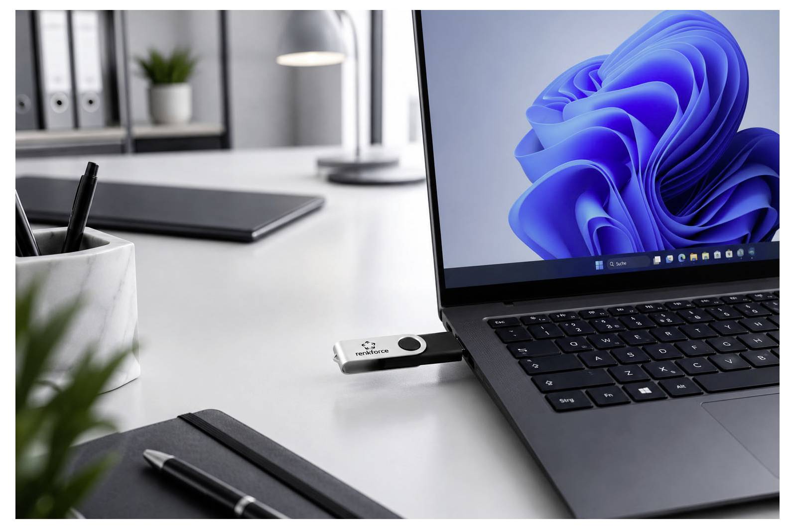 Ordinateur portable sur un bureau de bureau avec une clé USB insérée, affichant un écran de bureau Windows à côté de fournitures de bureau et d'un carnet de notes.