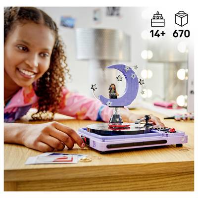 Fille souriante construisant un affichage de lune de style LEGO sur un ensemble de plateau tournant, avec des icônes « 14+ » et « 670 pièces » dans le coin.