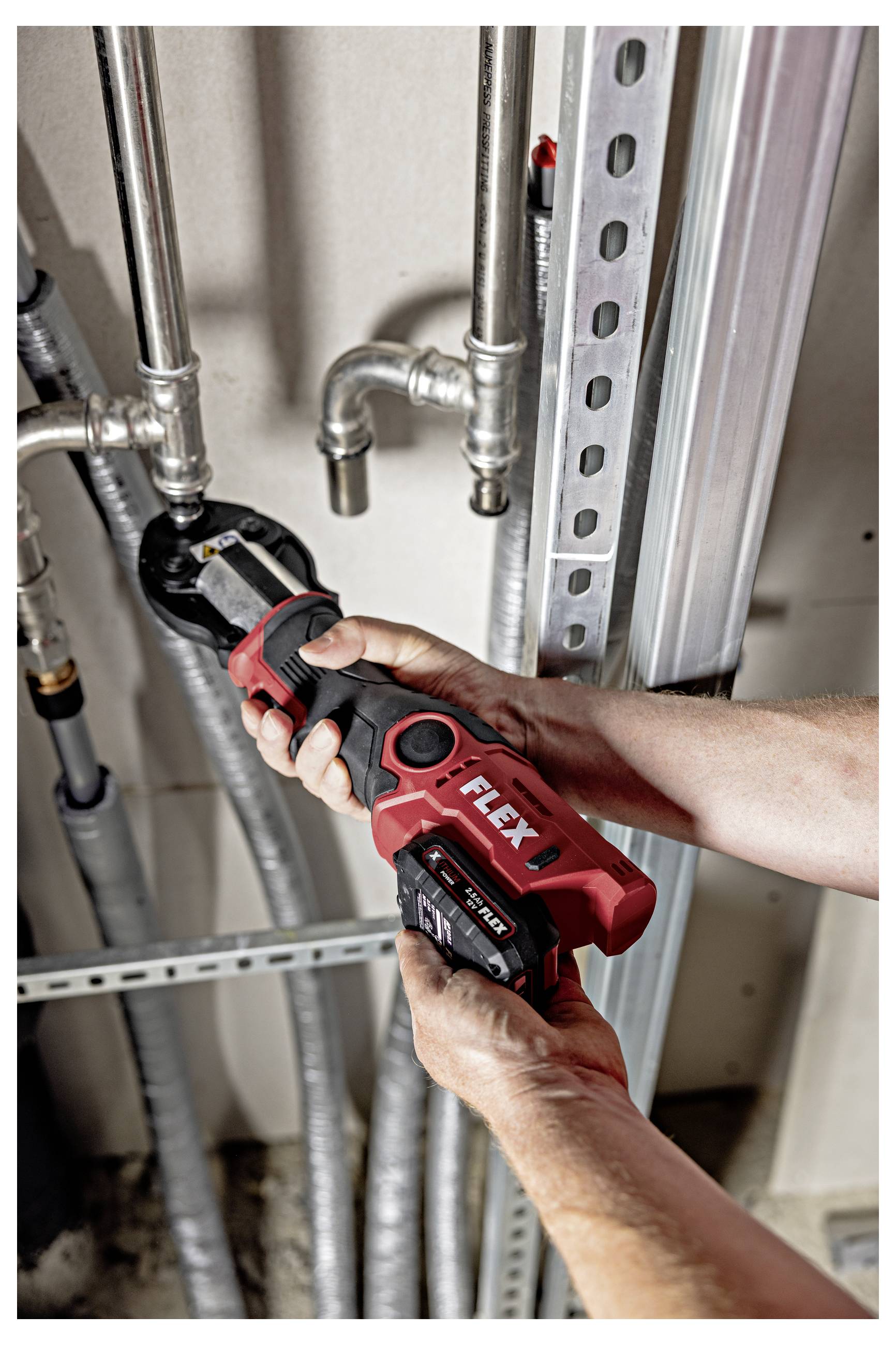 Personne utilisant un coupe-tube sans fil rouge sur des tuyaux de plomberie métalliques à l'intérieur d'une zone d'utilité/maintenance.
