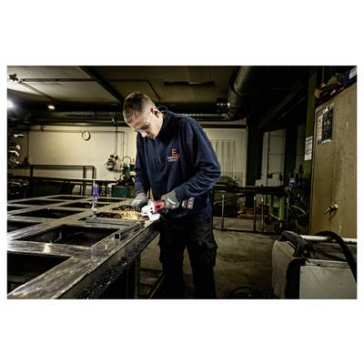 Un travailleur dans un atelier utilise une meuleuse d'angle sur un cadre métallique, avec des étincelles qui volent de la zone de coupe.