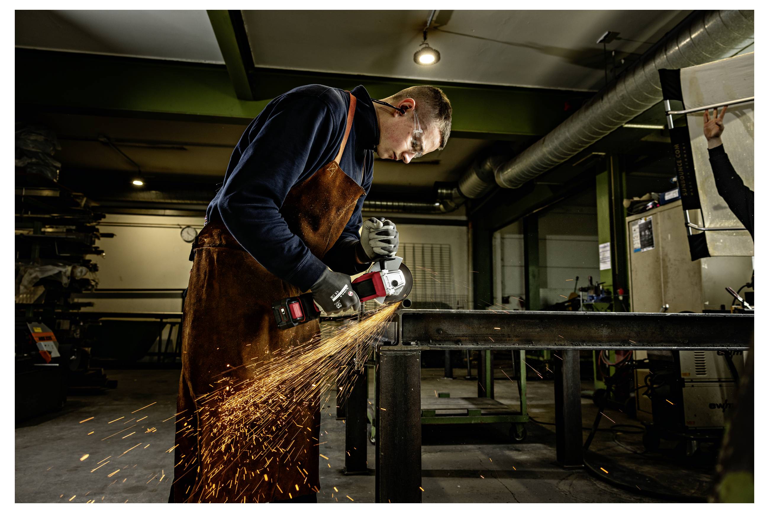 Un soudeur dans un atelier utilise une meuleuse d'angle sur un cadre métallique, projetant des étincelles brillantes.