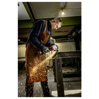 Homme en tablier et gants utilisant une meuleuse d'angle sur une table métallique, envoyant des étincelles brillantes dans un atelier.