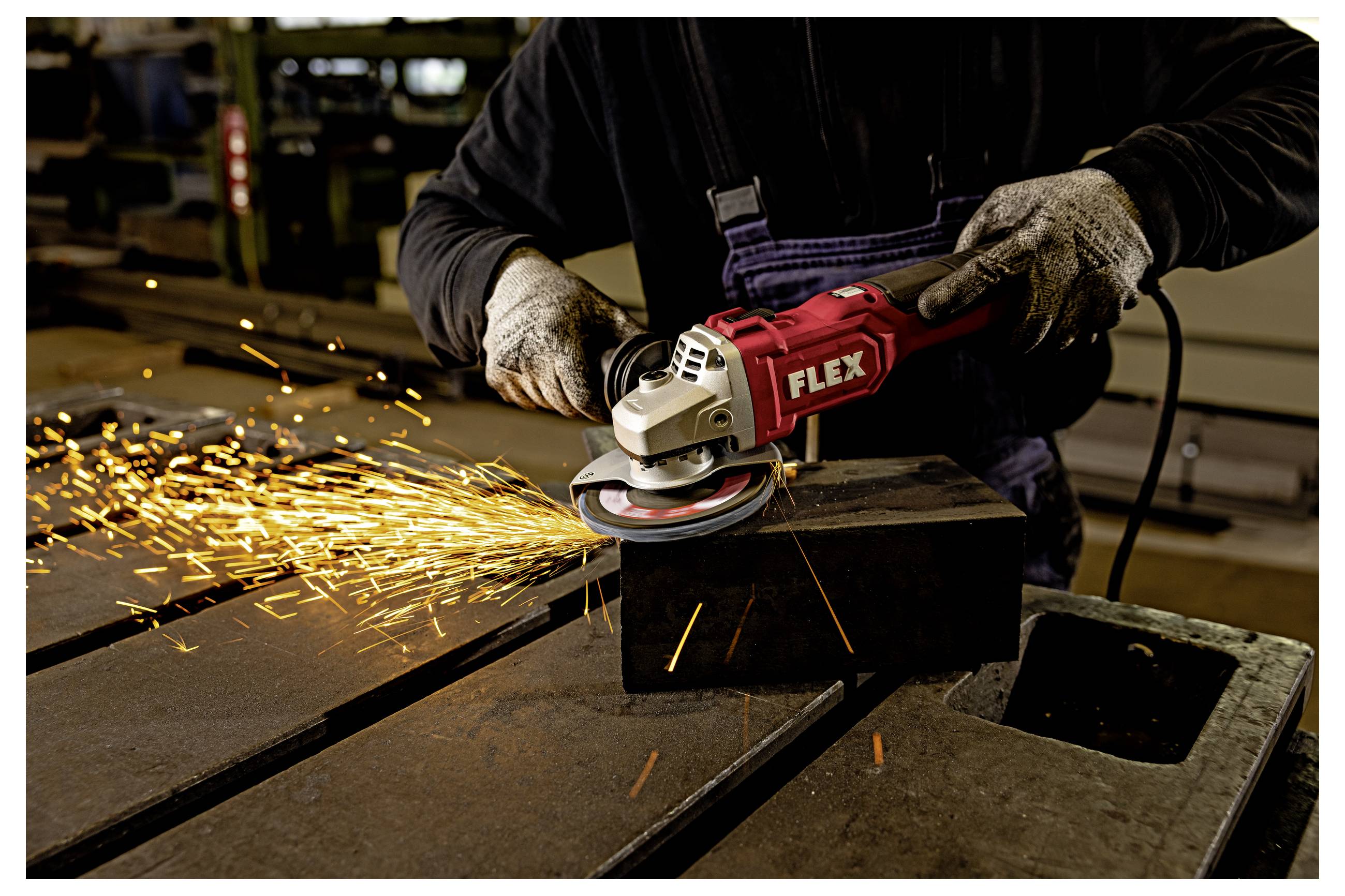 Travailleur utilisant une meuleuse d'angle FLEX rouge pour couper le métal sur un établi, avec des étincelles brillantes qui jaillissent dans un atelier.