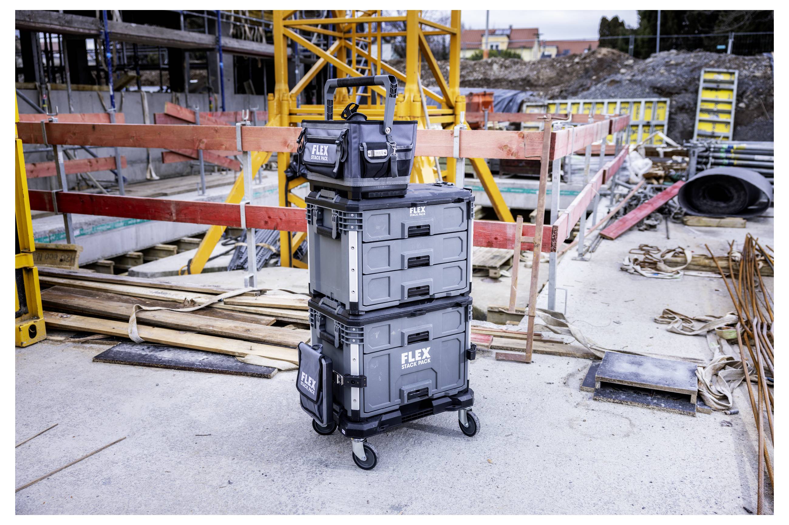 Caisses à outils FLEX empilées sur un chariot à roulettes sur un chantier de construction, avec du bois d'œuvre, des barrières et de l'équipement en arrière-plan.
