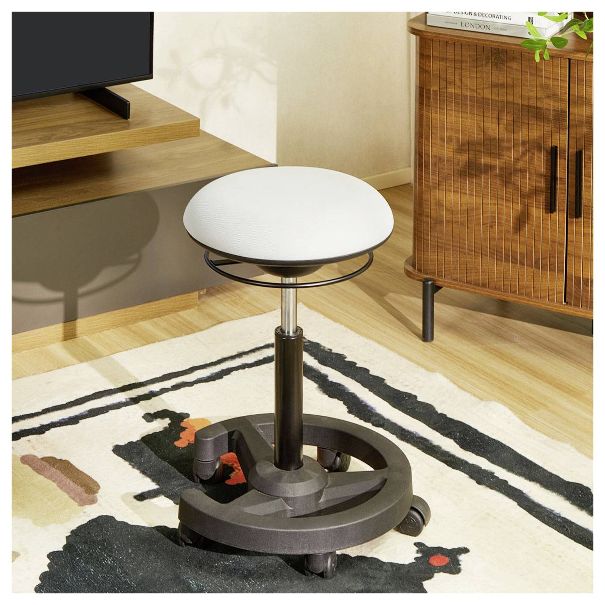 Tabouret rond ajustable avec siège blanc dans un salon moderne, à côté d'un meuble télé et d'une armoire en bois sur un tapis à motifs.