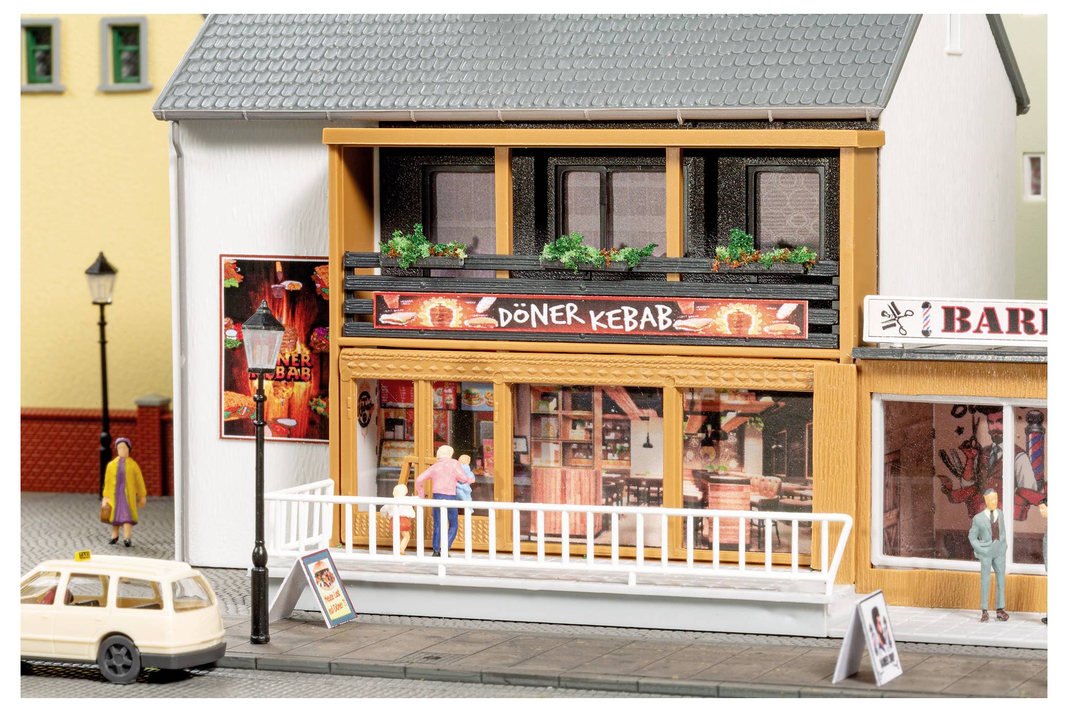Scène de rue miniature avec une devanture de magasin « DÖNER KEBAB », des piétons, une voiture garée et des devantures adjacentes sur la façade d'un bâtiment de maquette.