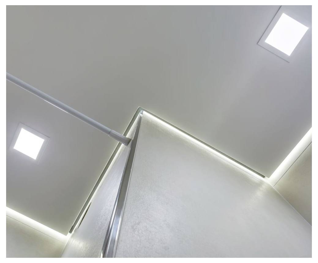 En levant les yeux vers un coin de plafond gris clair avec des lumières carrées encastrées et un éclairage à bande LED le long des bords.