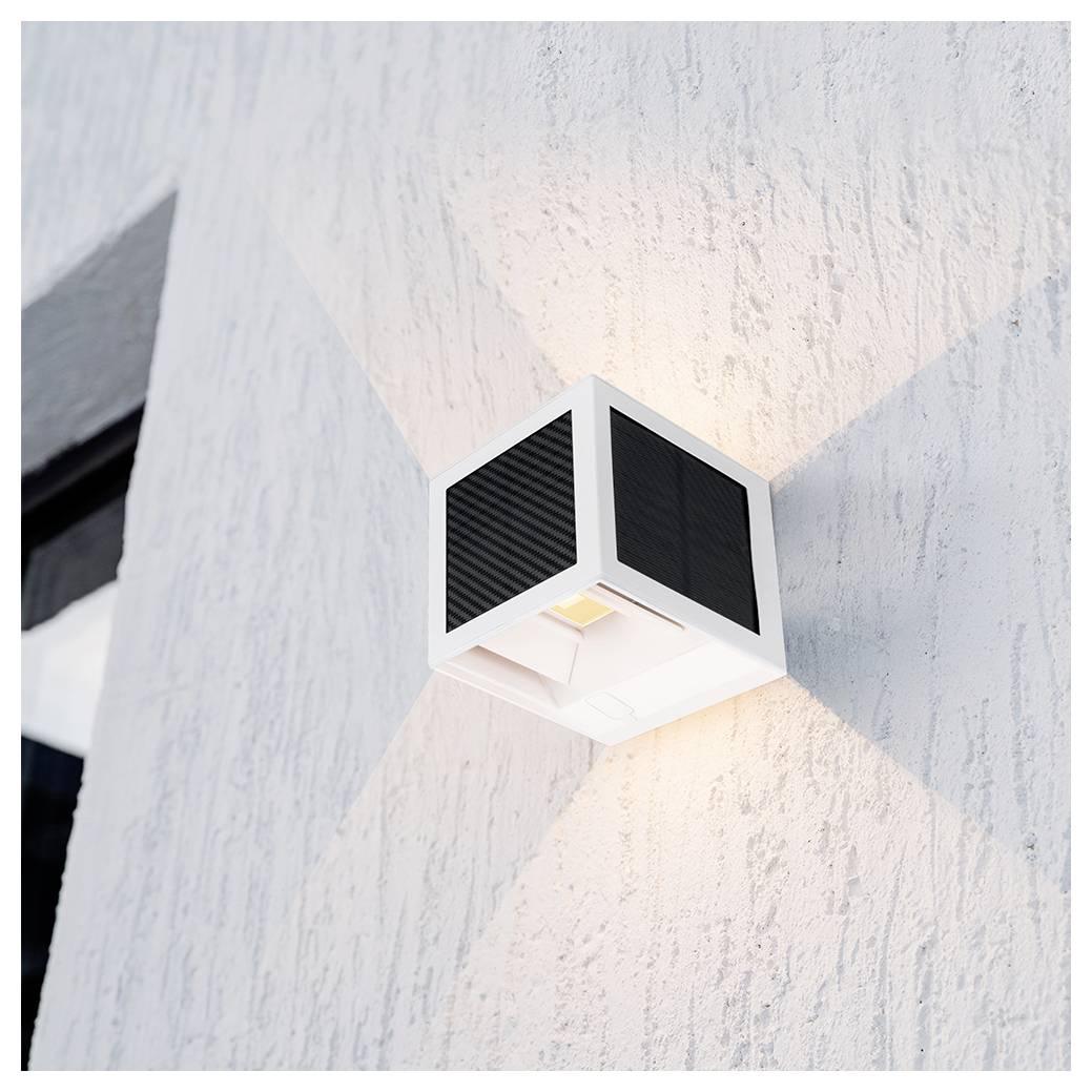Applique murale cubique moderne aux côtés à lames noires projetant une lumière chaleureuse sur un mur extérieur blanc texturé.
