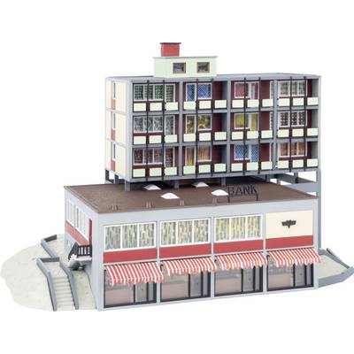 Un modèle d'un petit bâtiment bancaire avec des auvents rayés, surmonté d'un immeuble d'appartements multi-étages, présenté comme une maquette architecturale.