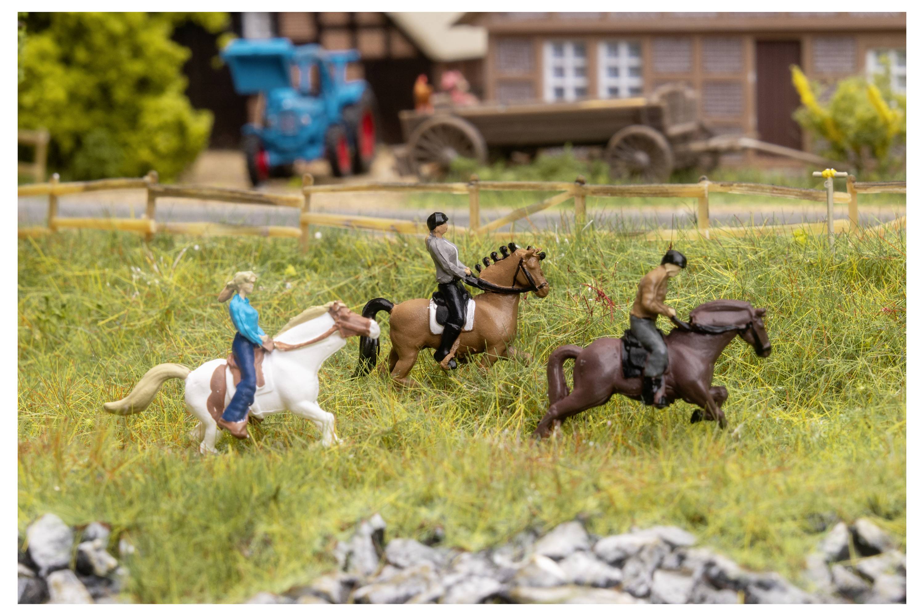 Scène miniature de trois cavaliers à cheval dans un champ herbeux, avec une clôture et des bâtiments de ferme en arrière-plan.