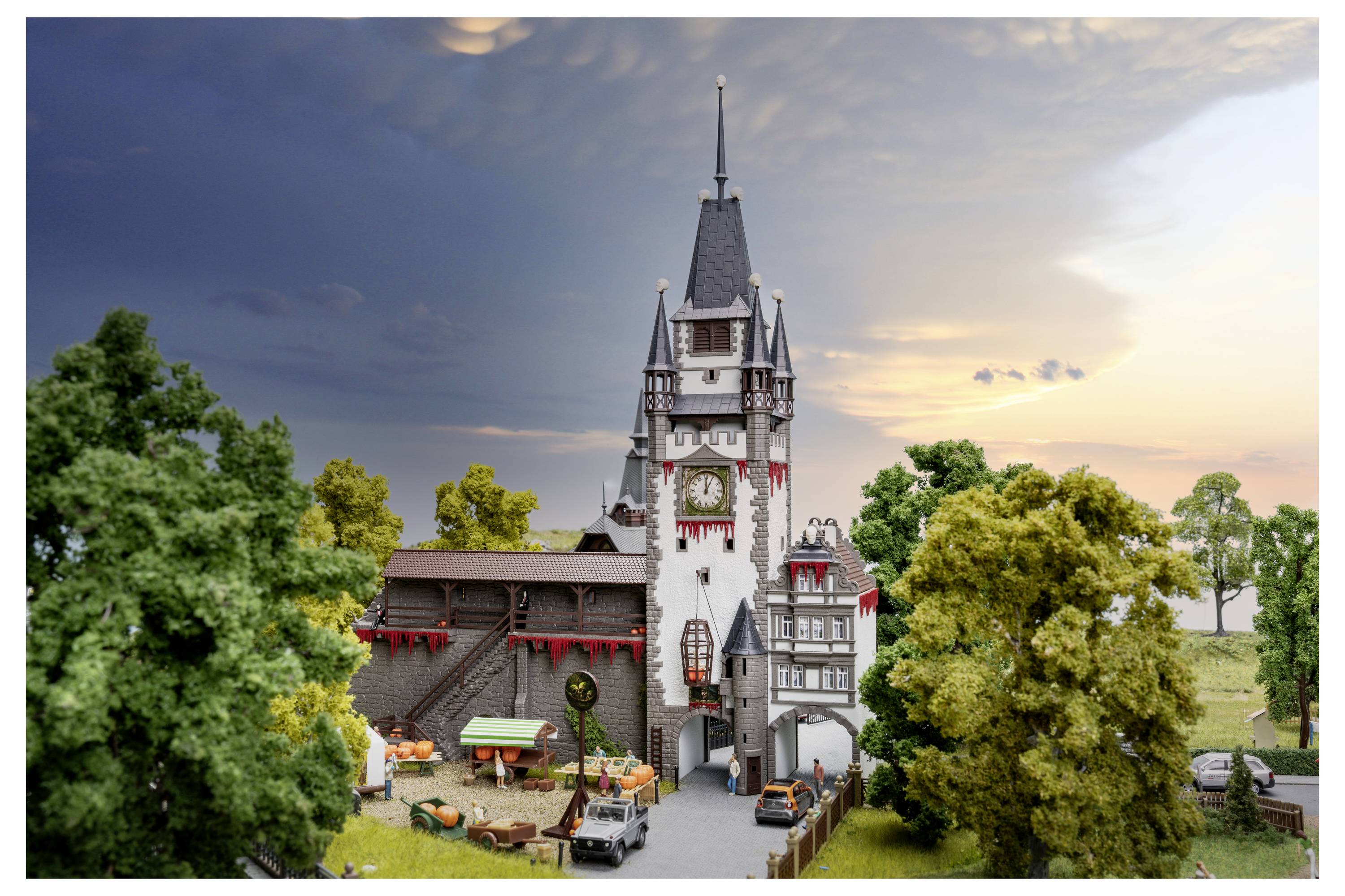 Un modèle miniature détaillé d'un bâtiment ressemblant à un château avec une haute tour, entouré d'arbres et de petites figurines au coucher du soleil.