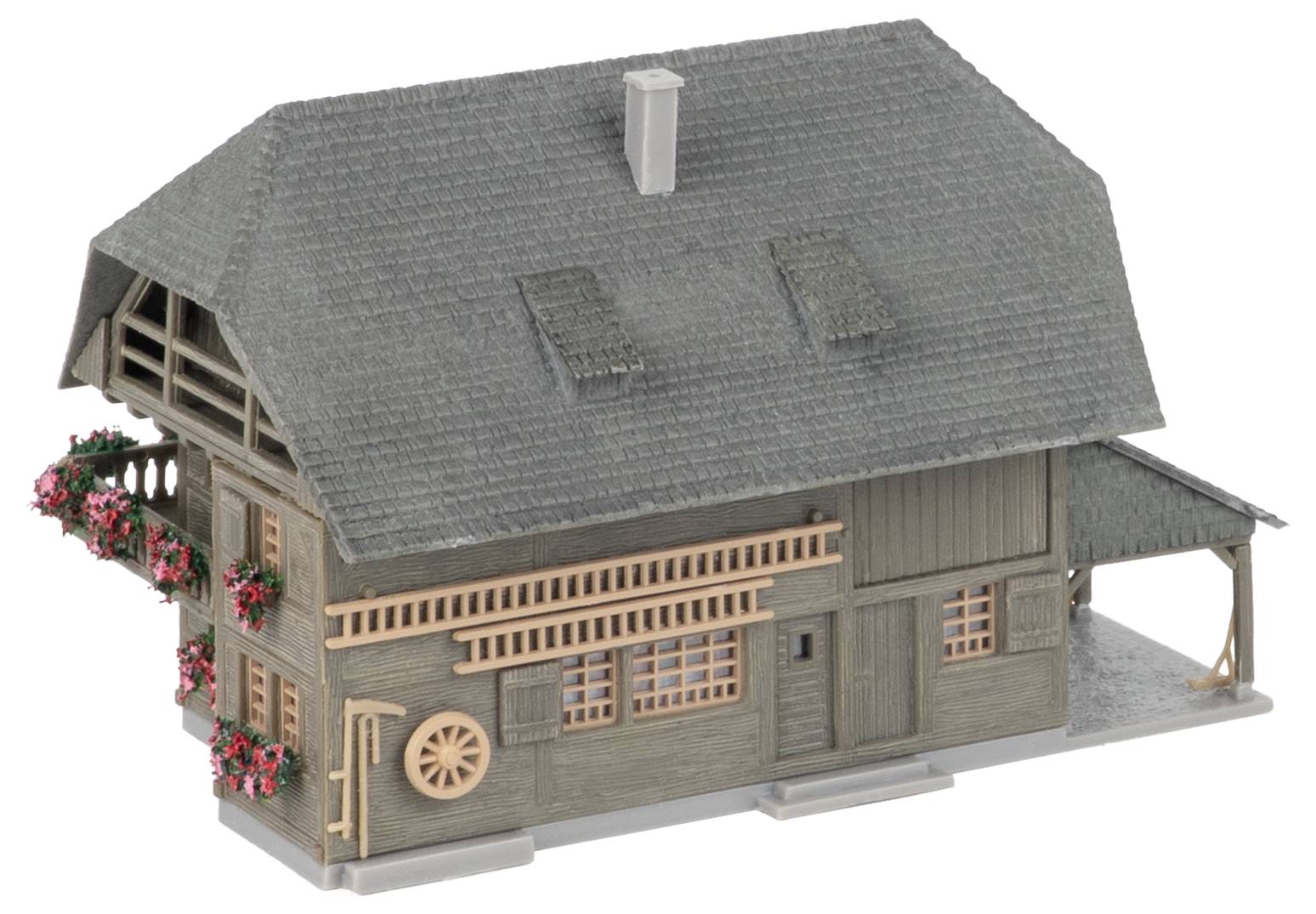 Modèle d'une maison rustique en bois avec toit à bardeaux gris, lucarnes, porche et jardinières de fleurs rouges, présenté sur fond blanc.
