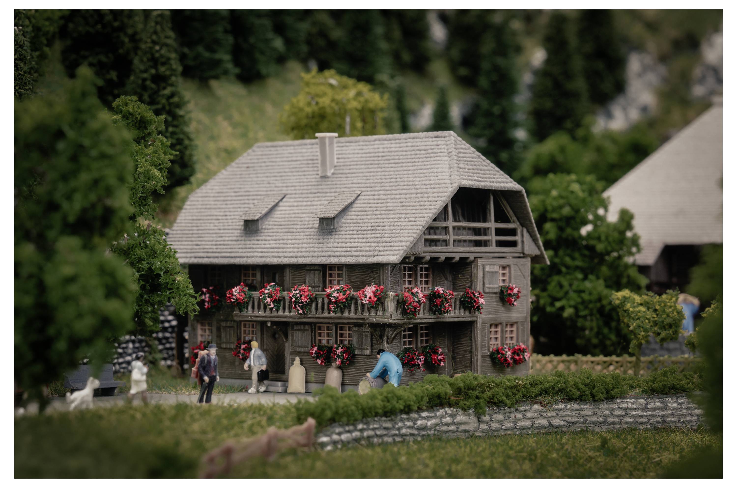 Un modèle miniature d'une maison décorée de fleurs avec de minuscules personnages dans une scène de village paysagé.