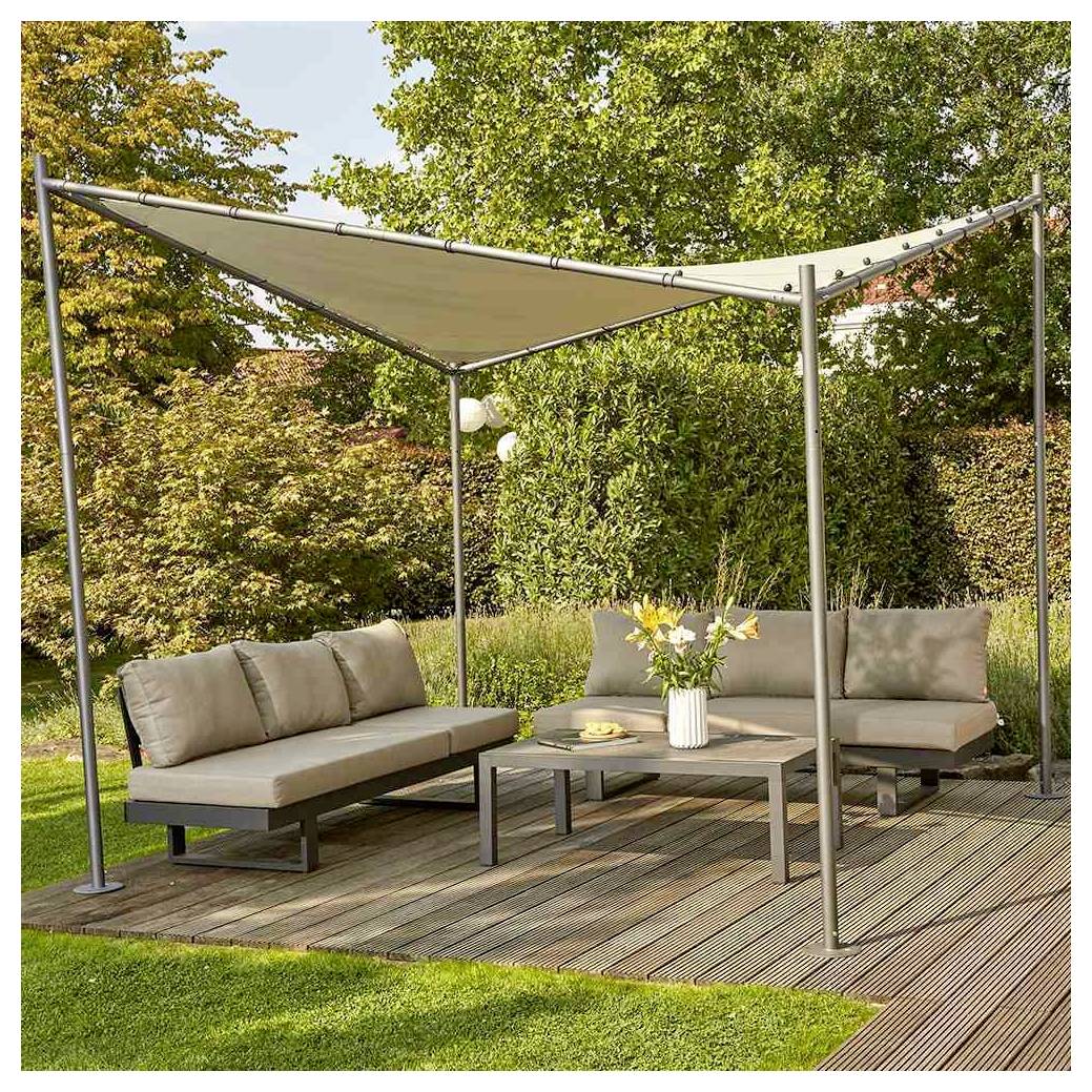 Zone de salle à manger extérieure avec deux canapés rembourrés, table basse, et auvent d'ombre triangulaire sur une terrasse en bois entourée de verdure de jardin.