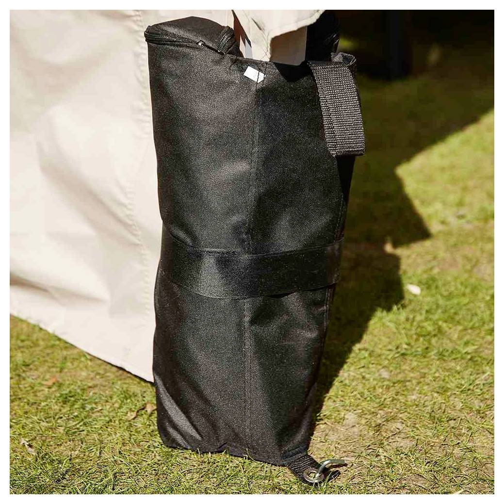 Sac cylindrique noir d'extérieur avec une sangle et un cordon de serrage repose sur l'herbe à côté d'une paroi de tente de couleur claire.