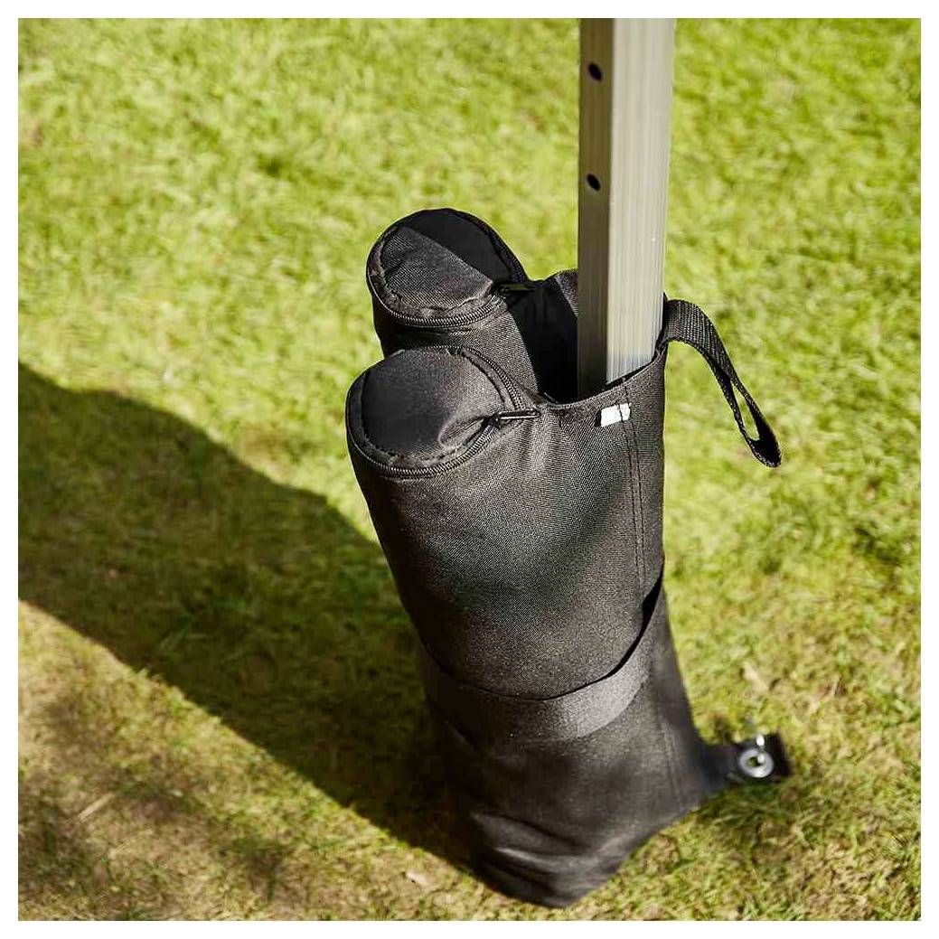 Sac de poids rembourré noir attaché autour d'un poteau vertical sur l'herbe, utilisé pour stabiliser un auvent ou une tente.