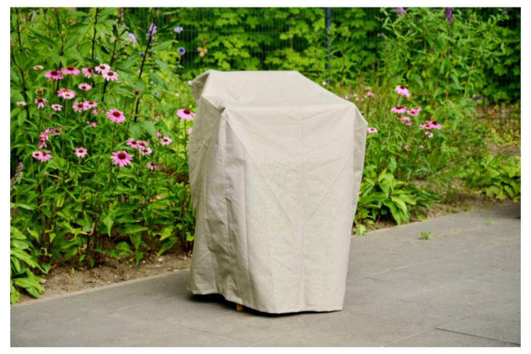 Une housse de protection beige drapée sur un objet extérieur sur un sentier pavé à côté de fleurs roses et de feuillage de jardin vert.