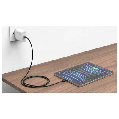 Tablette en charge sur un bureau en bois, connectée par un câble à une prise murale et affichant un écran abstrait coloré.