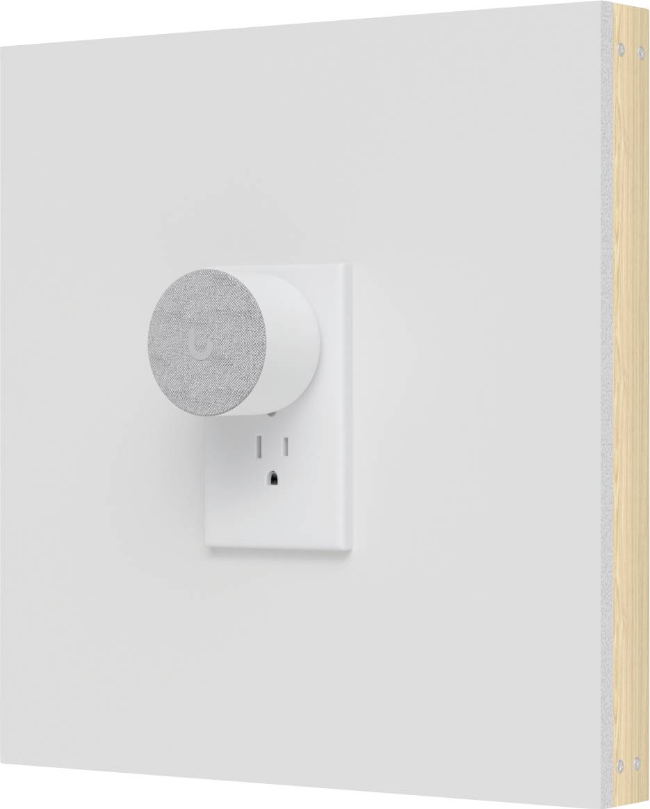 Prise intelligente murale blanche ou capteur avec façade circulaire grise sur une plaque de prise blanche, présenté contre un mur uni.