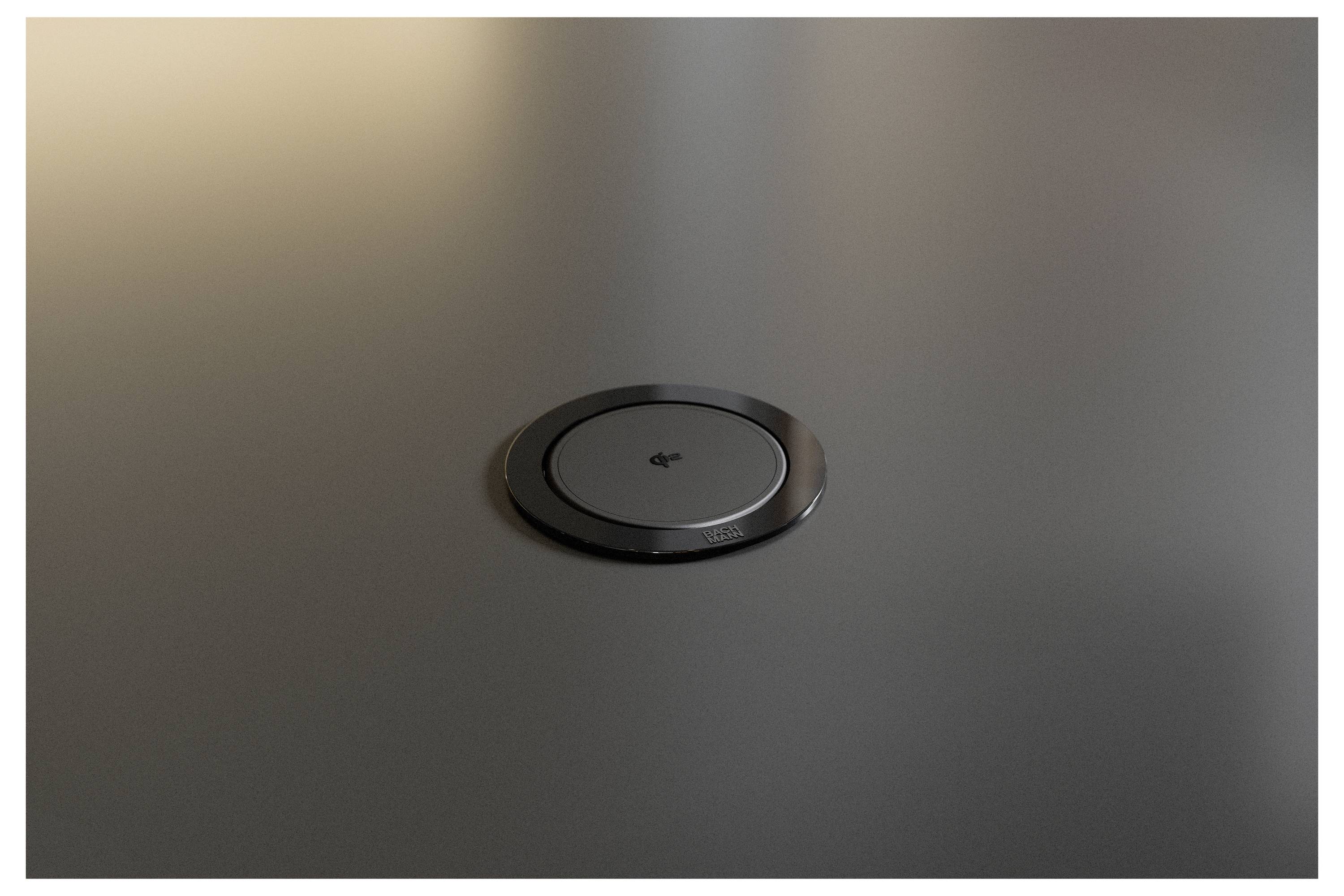 Un plateau sombre avec un dispositif rond noir ressemblant à un palet ou un dessous-de-verre au centre, éclairé par une lumière chaude provenant du coin supérieur gauche.