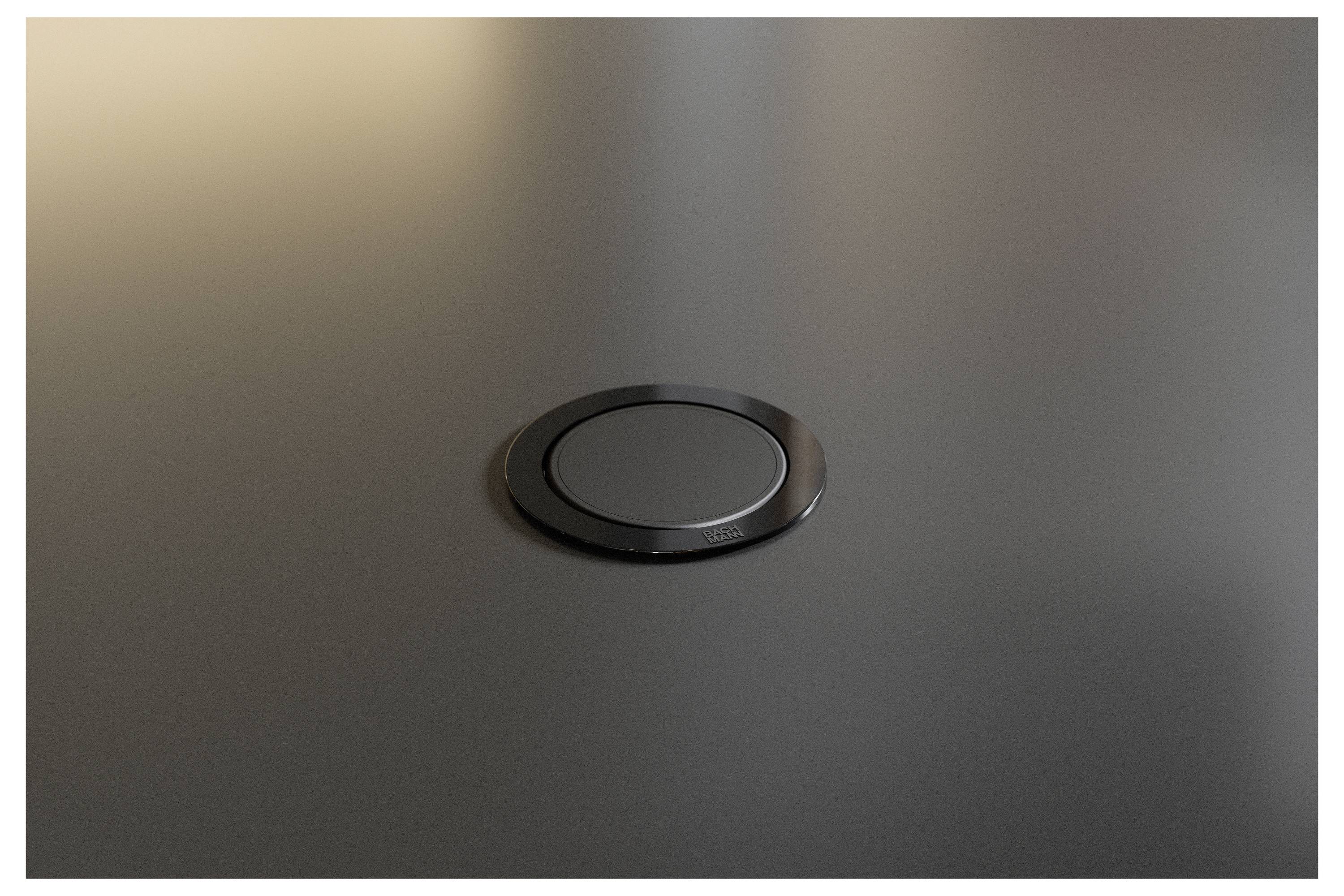 Gros plan d'une bague de table encastrée ronde noire ou d'un passe-câble sur une surface sombre.