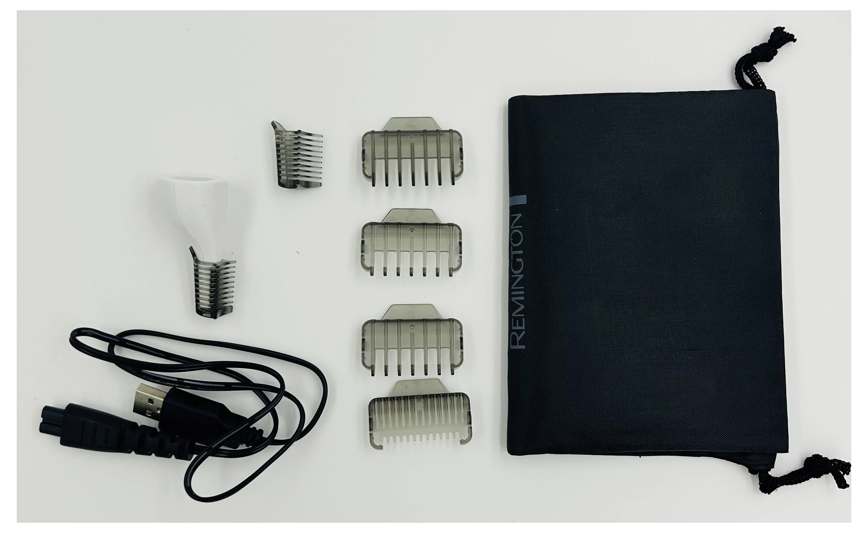 Kit de tondeuse à cheveux Remington avec étui noir, cordon de chargeur et plusieurs peignes de fixation arrangés sur une surface blanche.