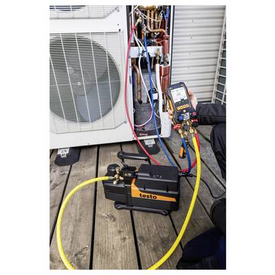 Technicien testant un climatiseur extérieur avec un manomètre Testo et des tuyaux connectés aux lignes de réfrigérant exposées de l'unité.