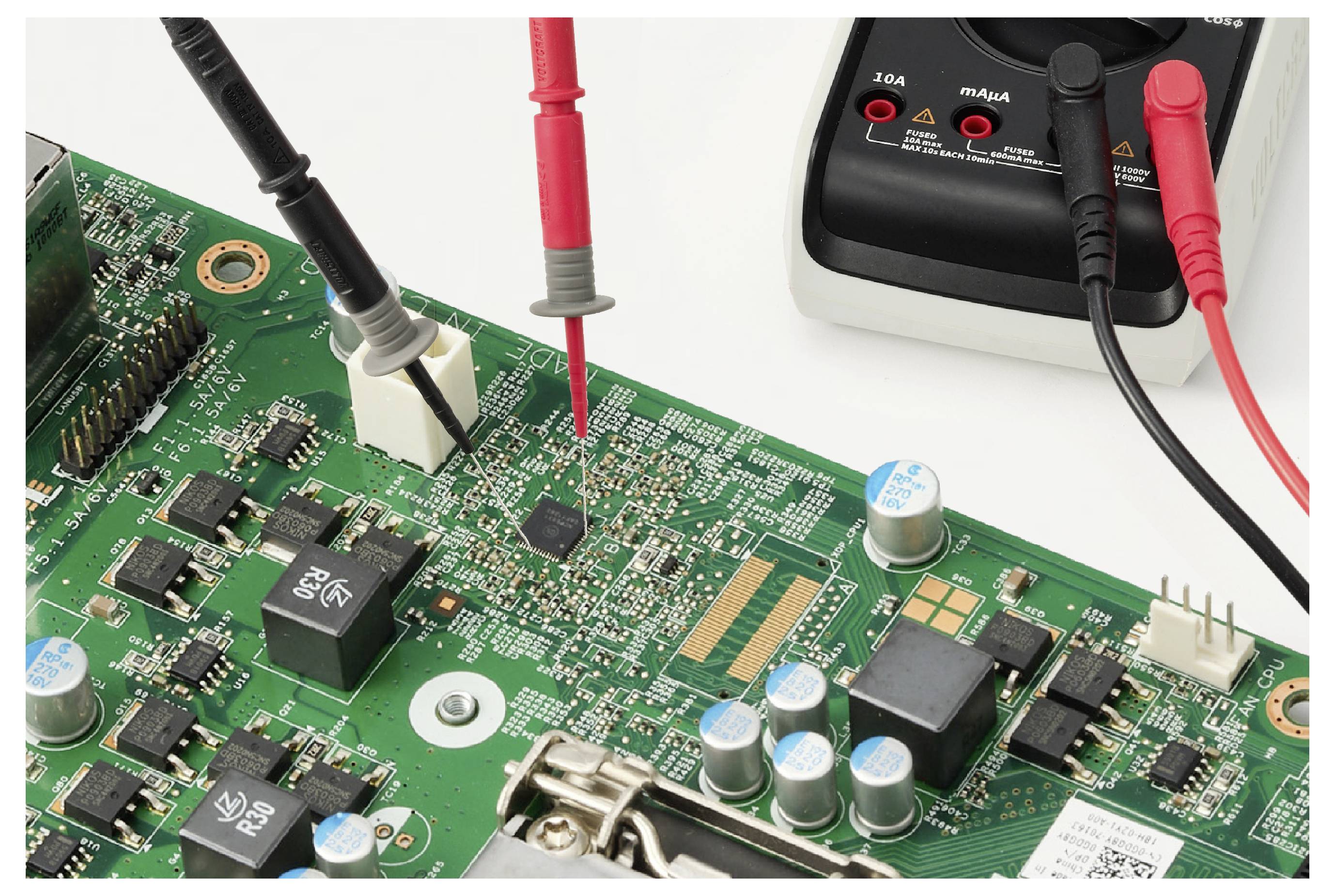 Les sondes d'un multimètre testent une carte de circuit imprimé verte, avec des fils rouge et noir connectés aux composants pour le diagnostic électronique.