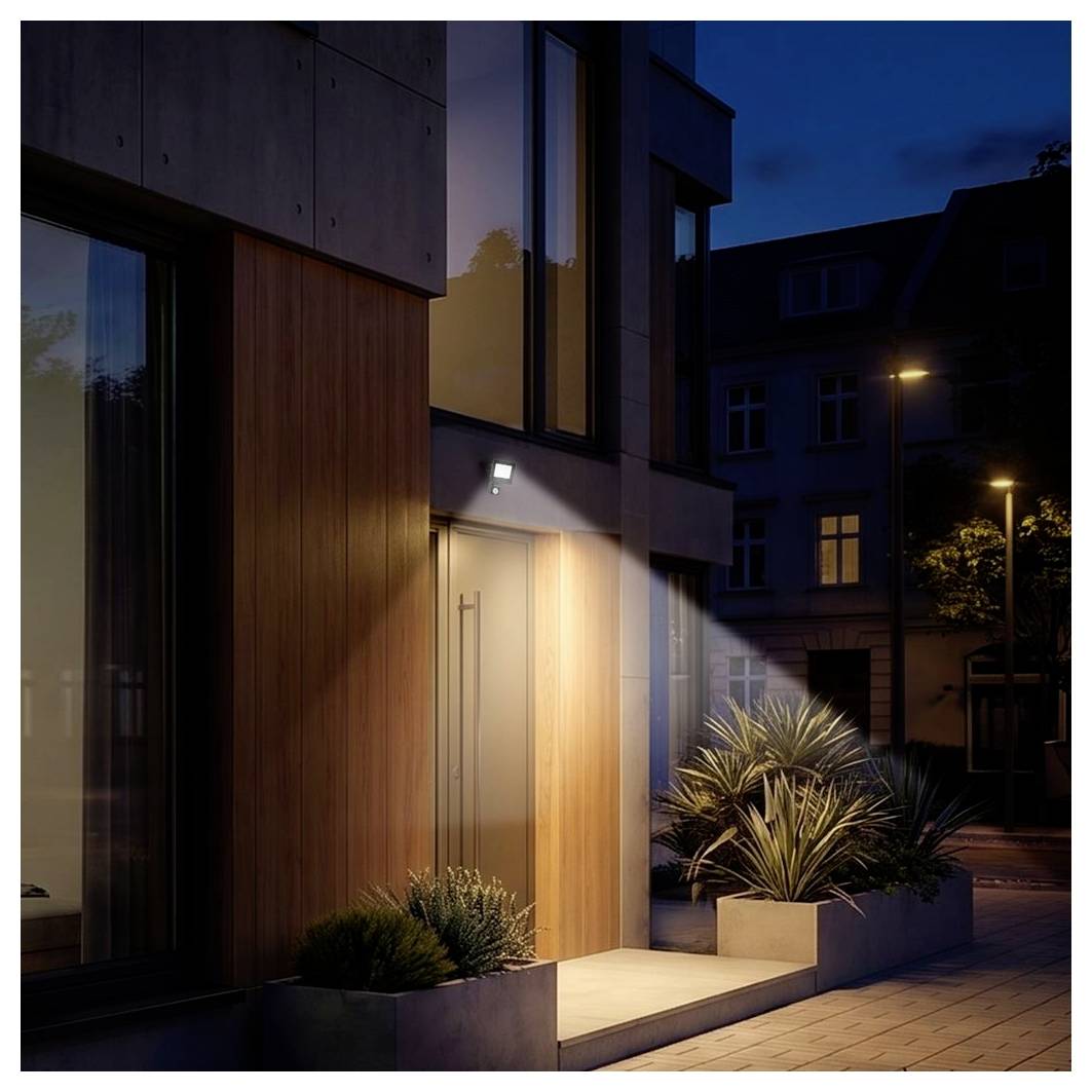 Entrée d'appartement moderne au crépuscule, porche chaleureusement illuminé avec façade en bois et verre, jardinières, et rue tranquille à l'extérieur.