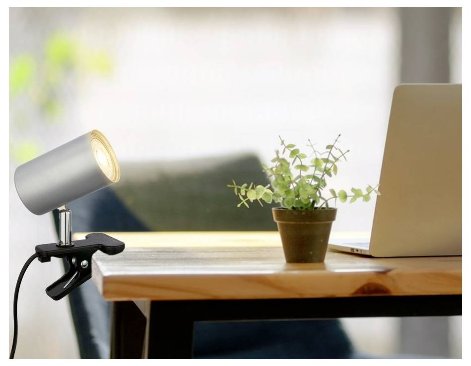 Lampe de bureau attachée à une table à côté d'une plante en pot et un ordinateur portable ouvert dans un environnement de bureau à domicile lumineux.