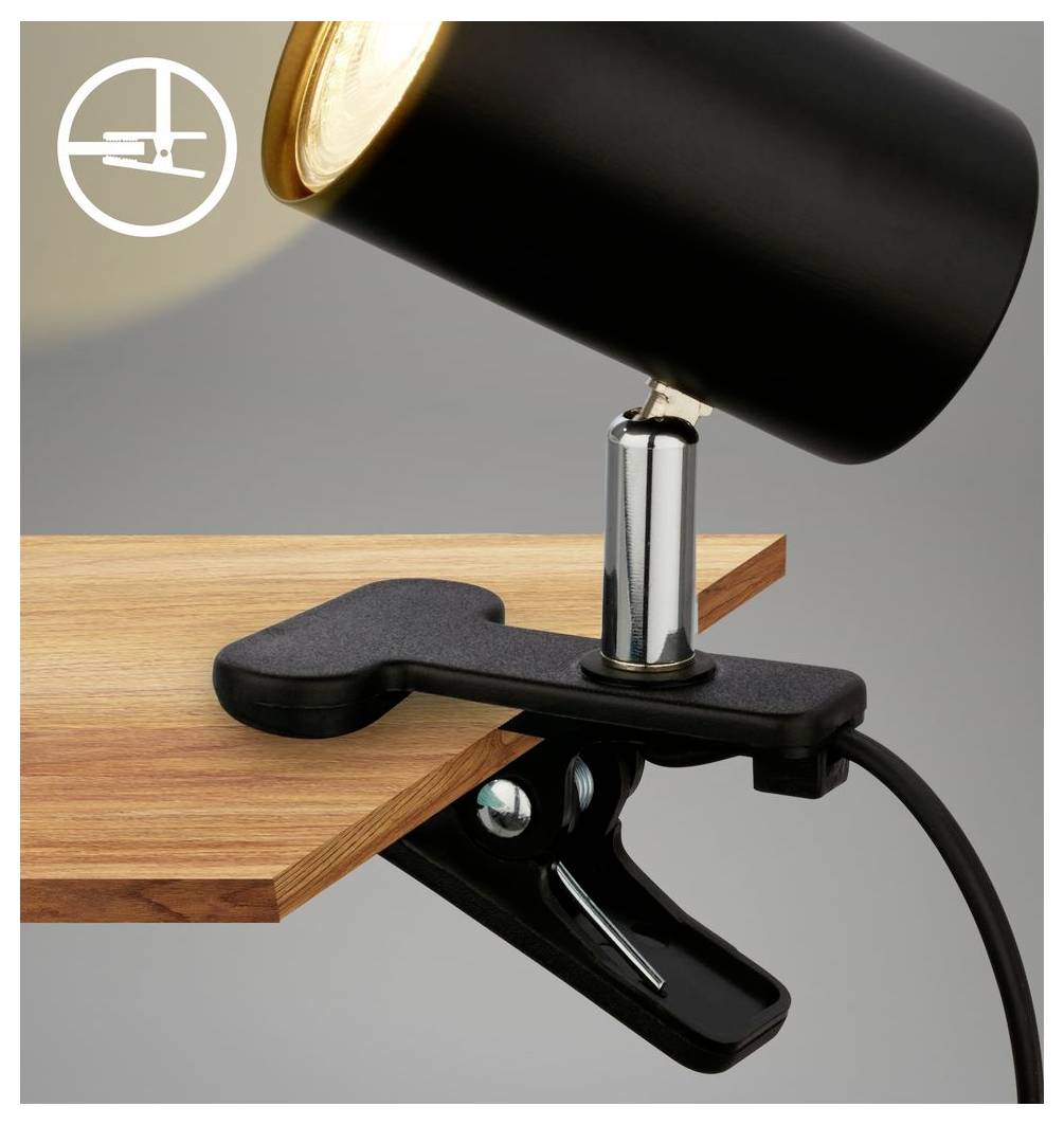 Lampe de bureau noire à pince fixée au bord d'une table en bois, avec une tête ajustable projetant la lumière vers le bas.