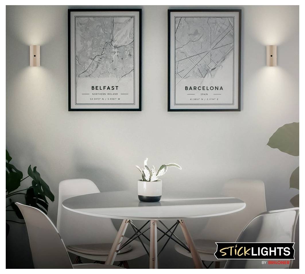 Coin repas moderne avec table ronde et chaises, deux cartes urbaines encadrées étiquetées « Belfast » et « Barcelone » sur le mur, et appliques murales.