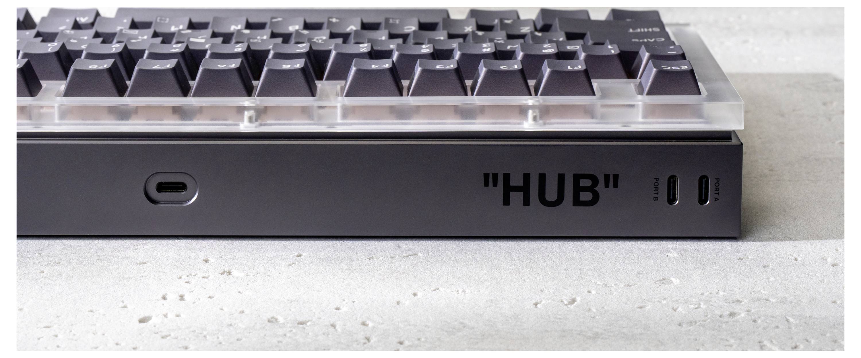 Gros plan d'un clavier connecté à un concentrateur métallique noir étiqueté « HUB », montrant les ports USB avant et une fente de câble.