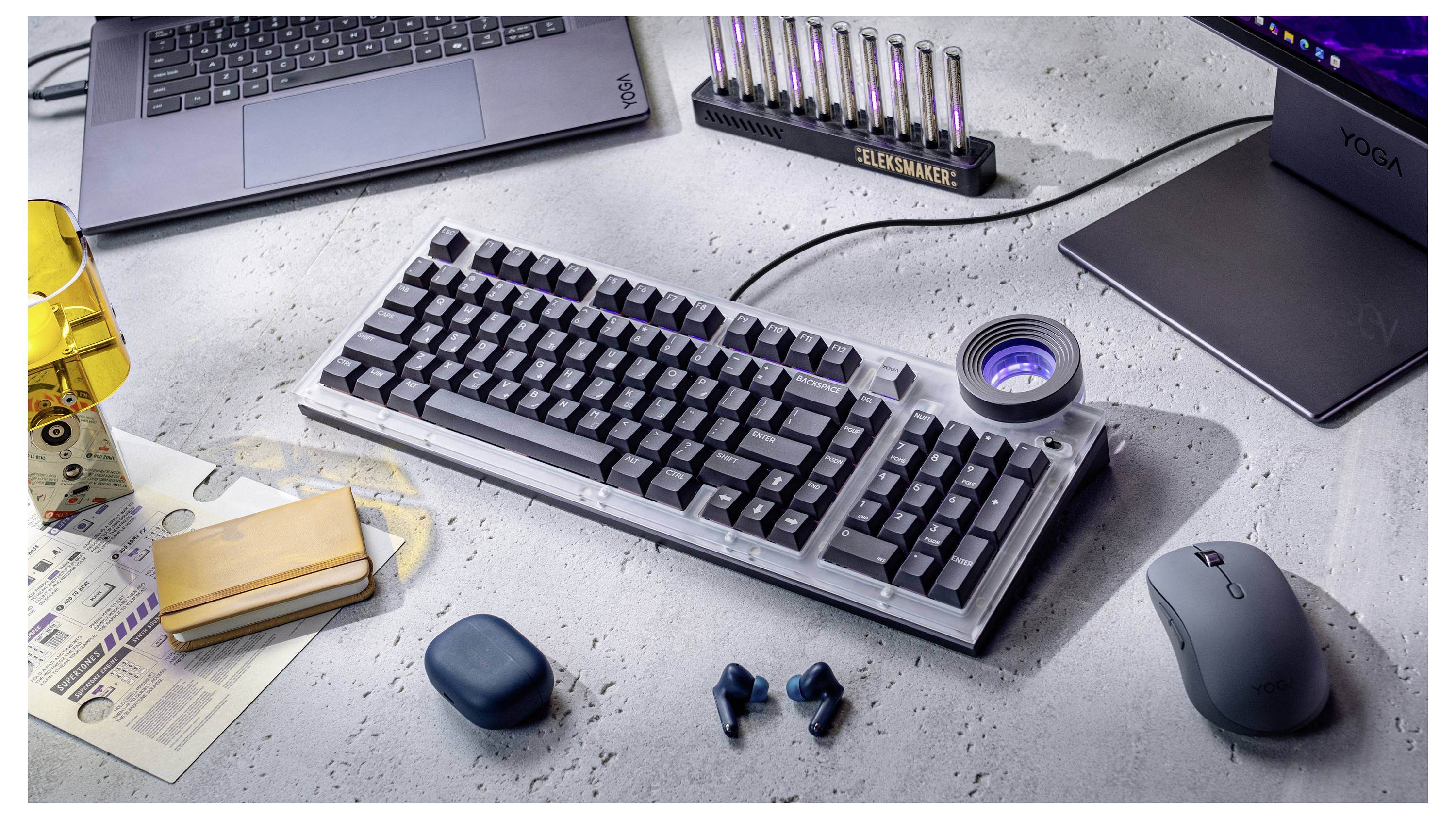 Un clavier mécanique sur un bureau avec un ordinateur portable, une souris sans fil, des écouteurs et de petits accessoires technologiques autour.
