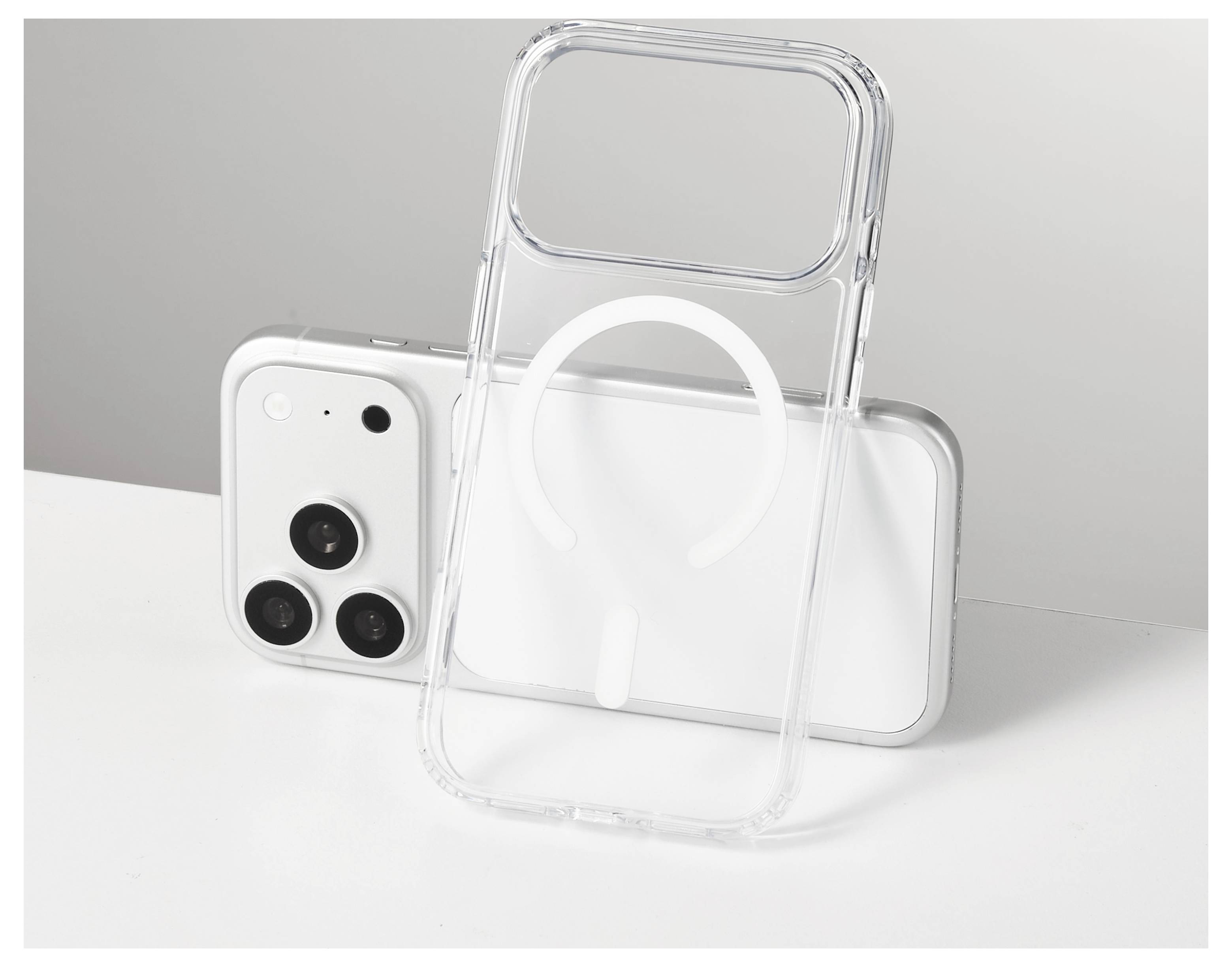Coque de téléphone transparent appuyée contre un smartphone blanc, présentant une grande bague de style MagSafe sur un plateau de table minimaliste.