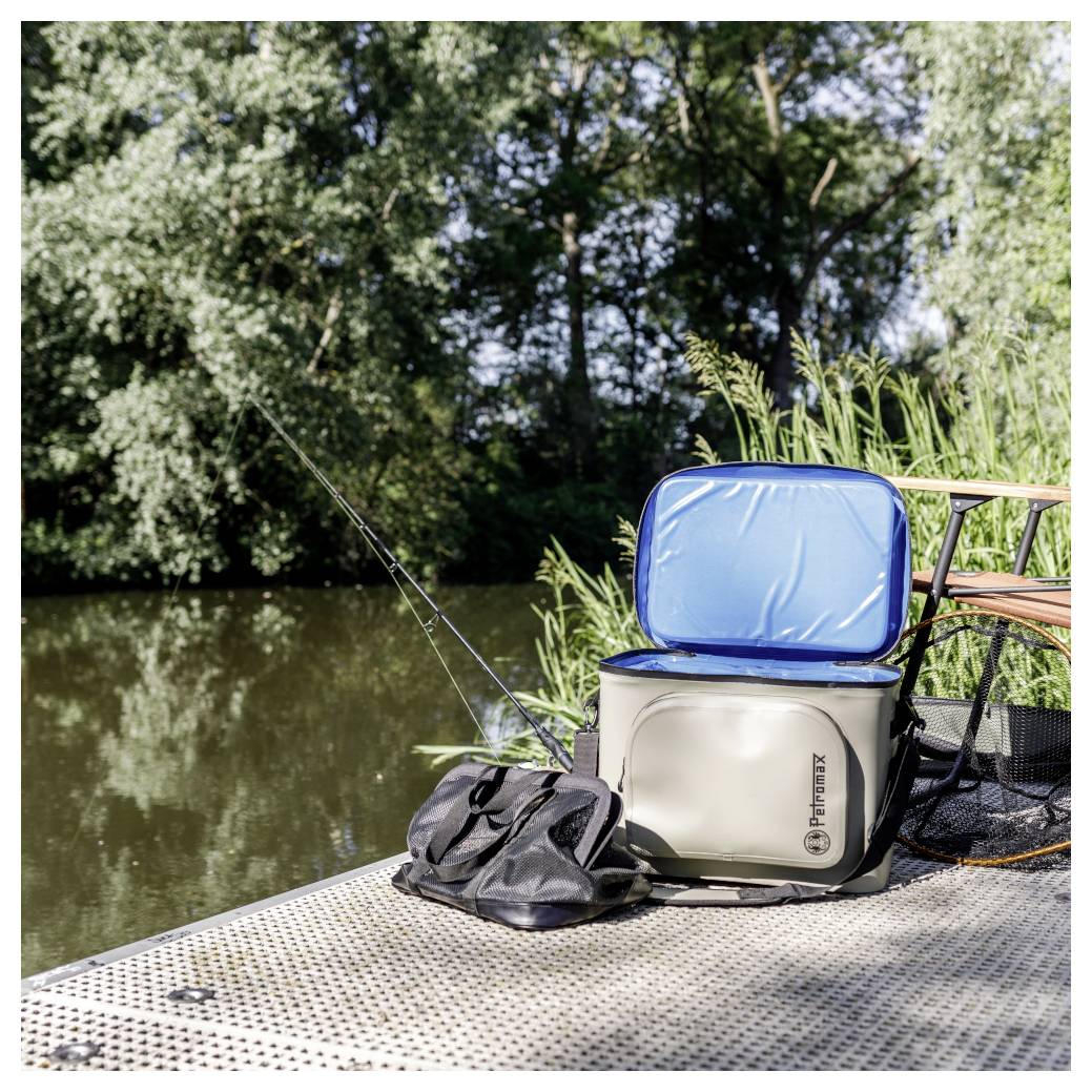 Équipement de pêche sur un quai près d'une rivière, avec une glacière, un sac et des cannes à pêche à côté de l'eau.