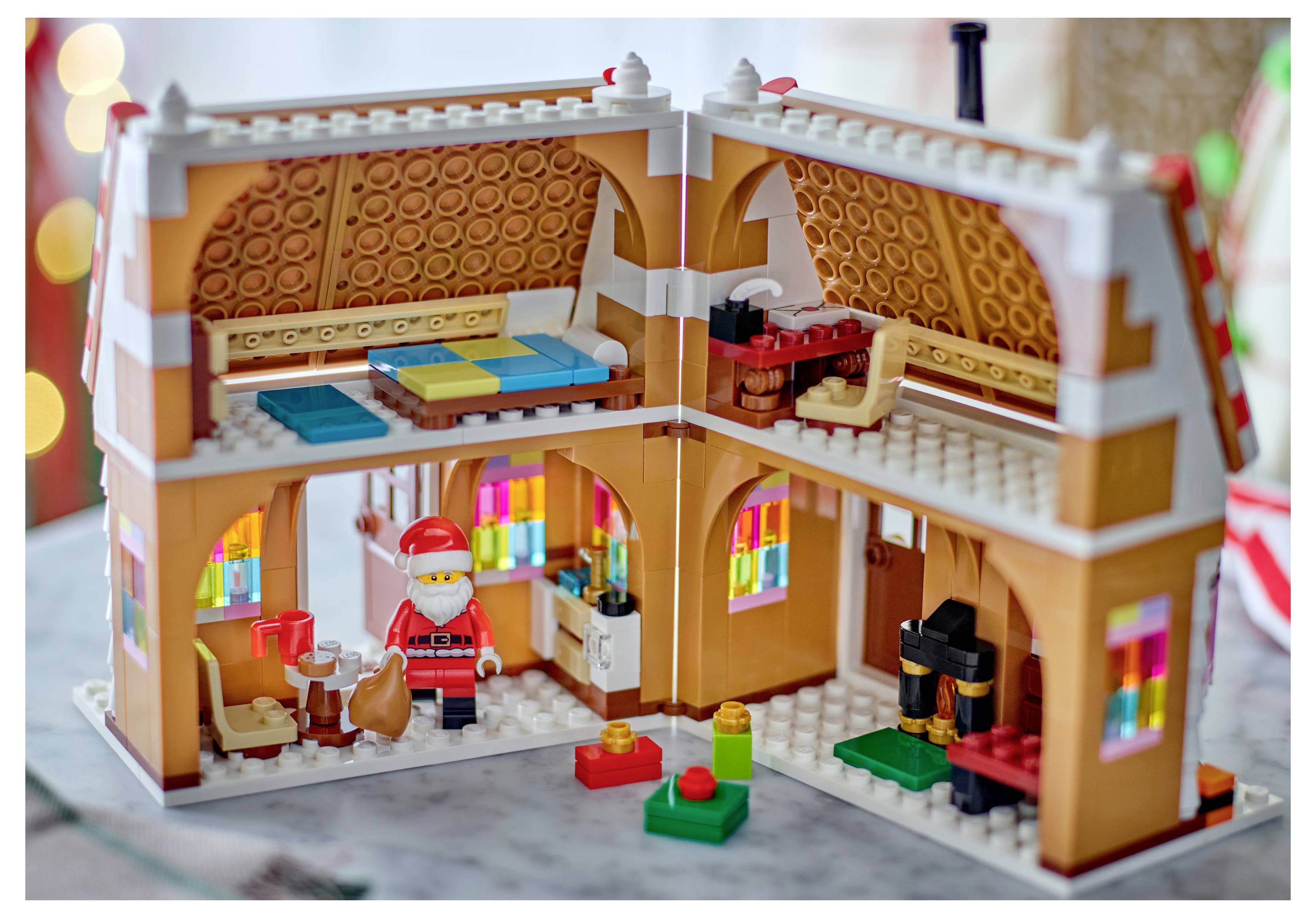 Maison de style LEGO en coupe montrant le Père Noël dans la pièce inférieure, un lit et des étagères à l'étage, et de petits accessoires festifs à l'intérieur.