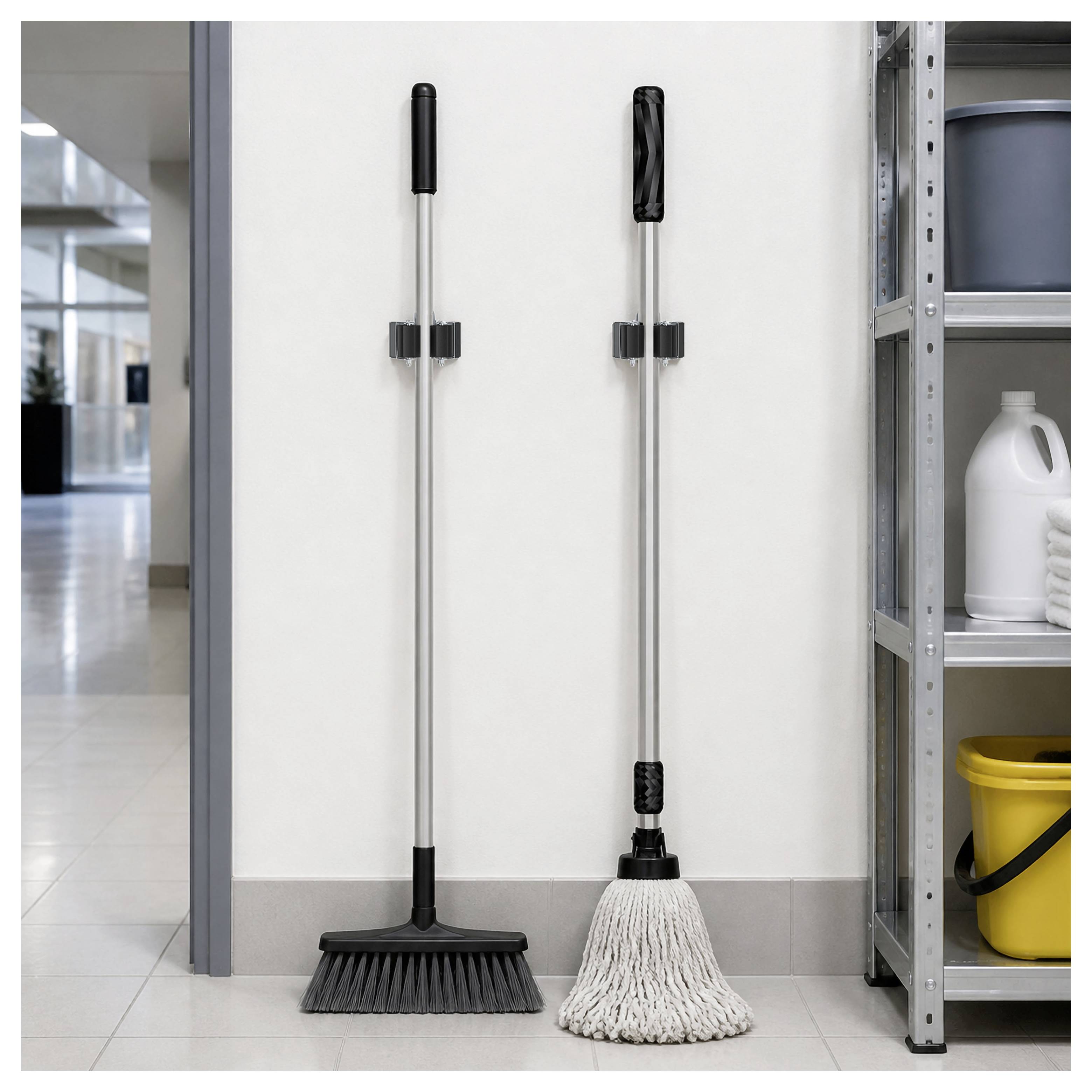 Deux outils de nettoyage—un balai et une vadrouille en ficelle—s'appuient contre un mur à côté d'une étagère de rangement contenant des produits de nettoyage.