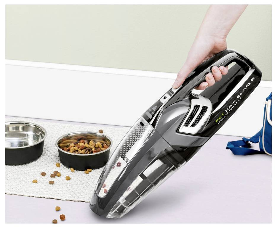 Aspirateur sans fil portatif nettoyant des aliments pour animaux de compagnie renversés à côté de deux bols pour animaux de compagnie sur un tapis de sol.
