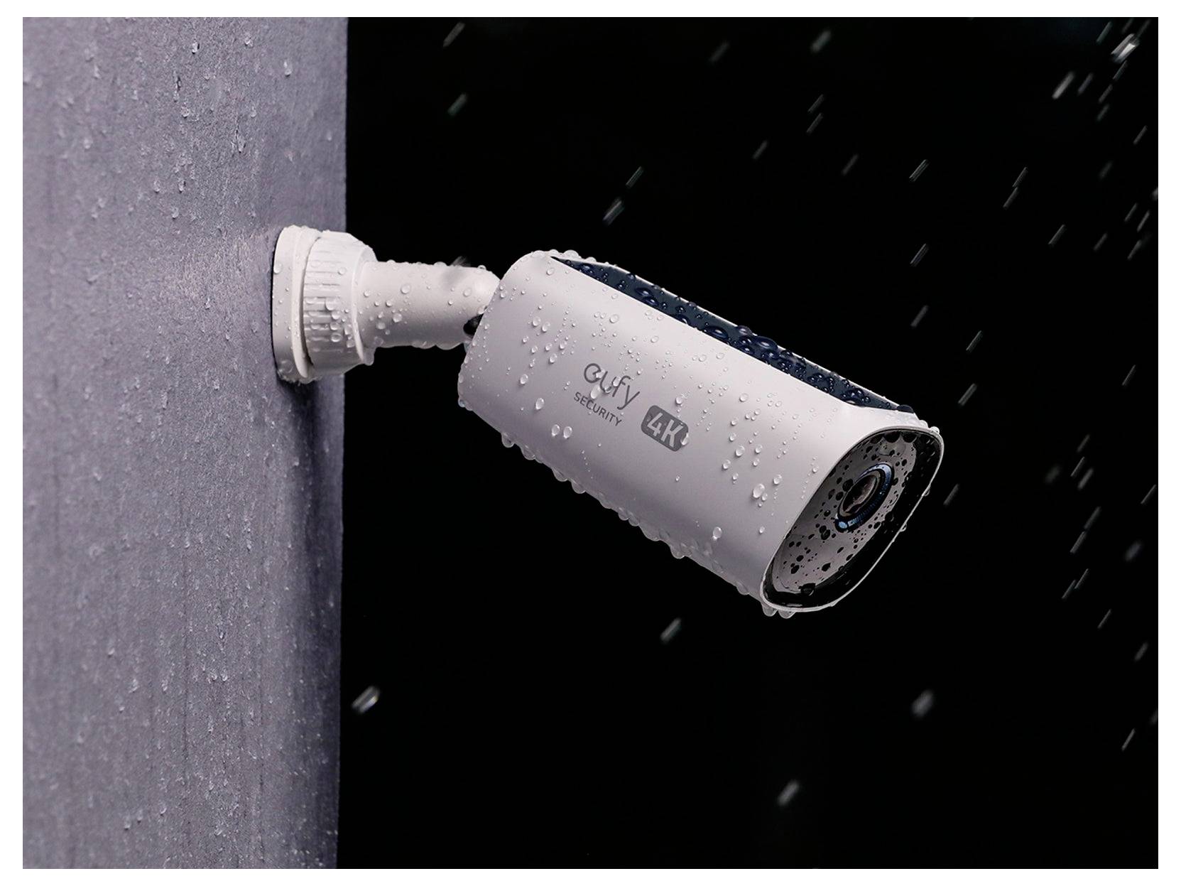 Caméra de sécurité extérieure blanche montée sur un mur, photographiée sous la pluie avec des gouttes d'eau visibles et le logo de marque « eufy 4K ».
