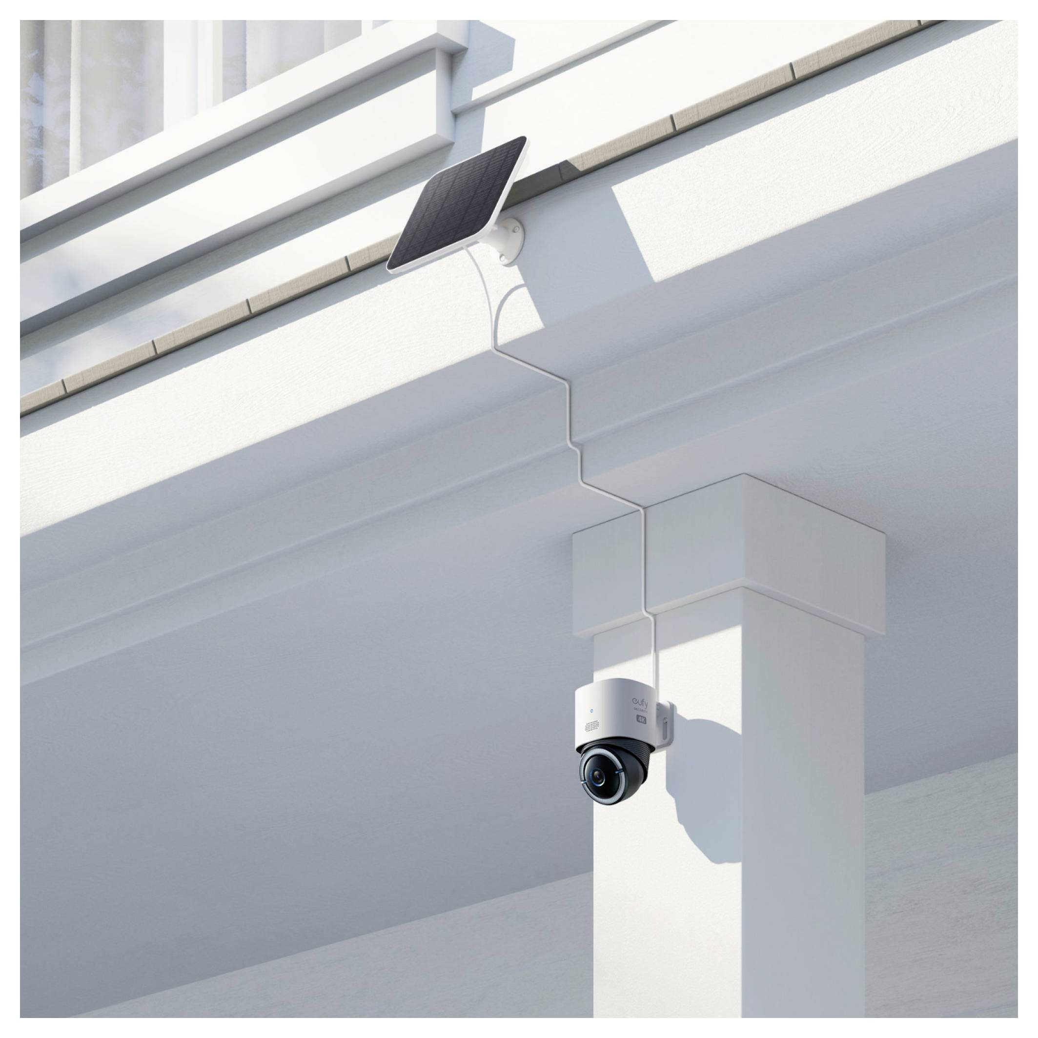 Caméra de sécurité alimentée par énergie solaire montée sur un pilier blanc d'un bâtiment sous un débord de toit.