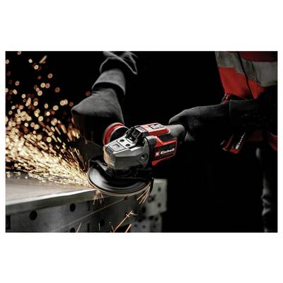 Un ouvrier utilise une meuleuse angulaire rouge pour couper le métal, envoyant des étincelles brillantes à travers une zone de travail industrielle sombre.