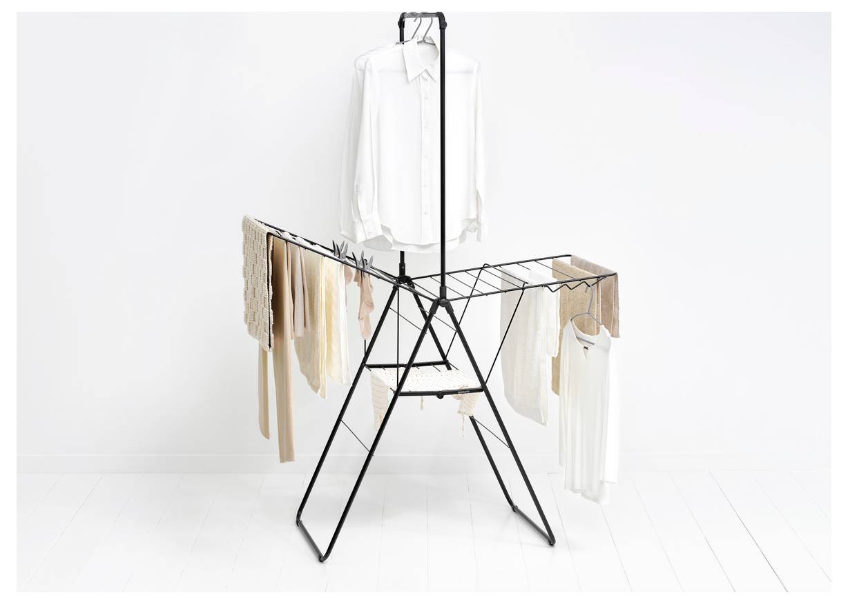 Un portant rotatif en métal noir affiche des vêtements blancs et beiges, y compris une chemise blanche sur le dessus, sur un fond de studio blanc.